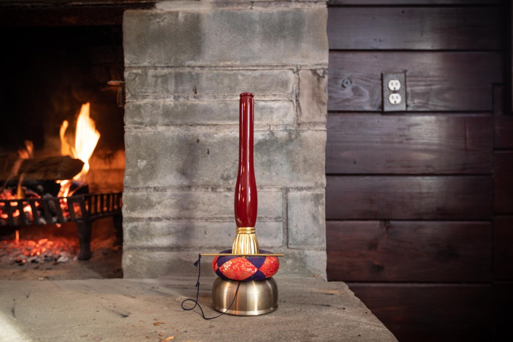 The incan bell sits next to the burning fireplace.